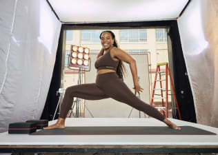 In this image for an article about how gym clothes affect motivation and performance, Peloton instructor Chelsea Jackson Roberts is grinning while doing a forward lunge in a matching brown activewear set.